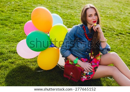 young stylish hipster teen girl happy smiling, park, air balloons birthday party, cool accessories, red lipstick makeup, colorful, sunny, have fun, sitting on grass, denim shirt, horizontal