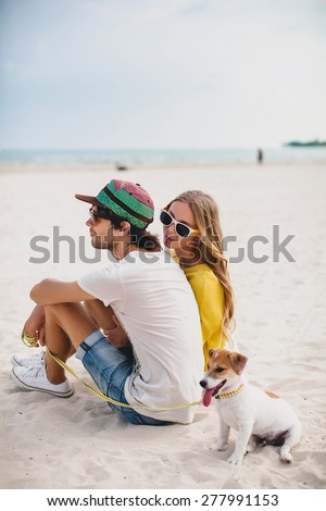 young stylish hipster couple in love walking playing dog puppy jack russell in tropical beach, white sand, cool outfit, romantic mood, having fun, sunny, man woman together, vacation