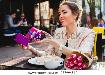 young stylish woman, sitting in cafe, holding present box, smiling, enjoying warm, tulips, happy birthday party, city street, europe vacation, horizontal, glamour outfit, romantic dinner