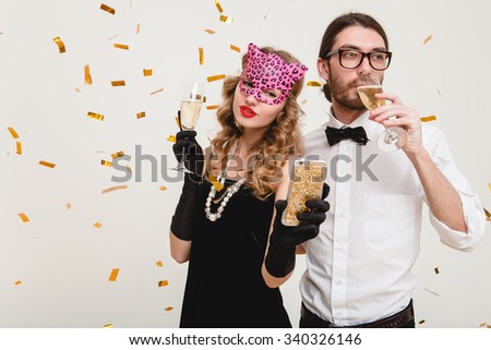 young stylish couple in love on white background holding glasses and drinking champagne, making self photo, celebrating new year, wearing black dress, mask, happy carnival disco party, having fun