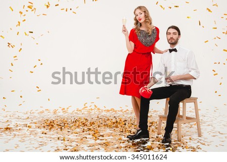 young stylish couple in love drinking champagne, celebrating new year, happy disco party, fashion luxury style, red dress, golden confetti, making presents, holding gift box, white background