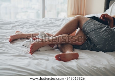young sexy couple in love lying in bed in hotel, embracing on white sheets, close up legs, romantic mood