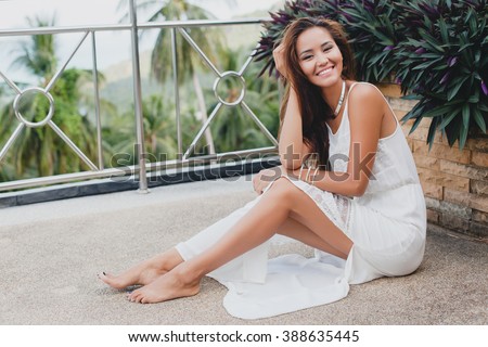 young stylish asian woman sitting on floor in white boho dress, vintage style, natural, pure, innocent, smiling, happy, skinny legs, tropical vacation, hotel, honey moon, barefoot