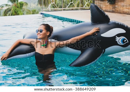 young beautiful stylish asian woman in pool, black swimming suit, inflatable pool toy, orca, summer swimwear, feather earring, sunglasses, tropical villa, vacation, skinny slim body