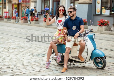 young beautiful hipster couple riding on motorbike city street, summer europe vacation, traveling, romance, smiling, happy, having fun, sunglasses, stylish outfit, together in love, adventures, date