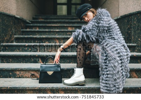 stylish woman in rich fur coat in city street, autumn fashion trend, black leather purse, cap, white boots, urban style, accessories, legs, footwear