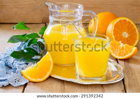 Orange juice in a glass and pitcher with mint, fresh fruits on wooden background