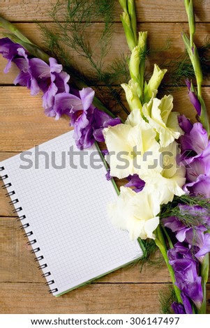 Flowers blue and white gladiolus with a notebook on a wooden table