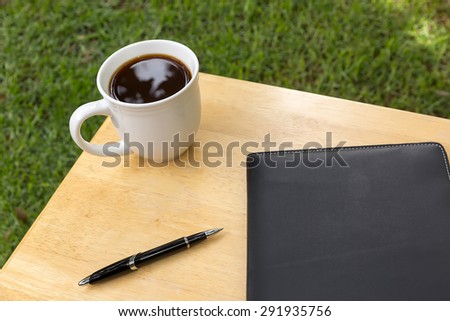 cup of coffee  with a book and a black on a wooden table in the garden
