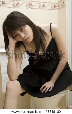 stock photo Sad Asian girl sitting on toilet bowl