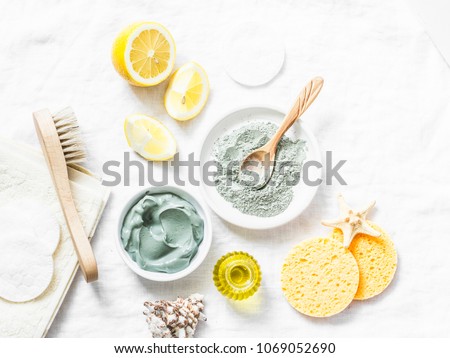 Homemade beauty facial mask. Clay, lemon, oil, facial brush - beauty products ingredients on light background, top view