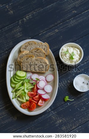 ingredients for whole wheat toasts with cheese, radish, cucumber, cherry tomatoes on dark wooden background