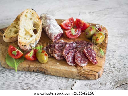 delicious appetizers for wine - Italian sausage, olives, tomatoes and ciabatta on olive Board on a light background