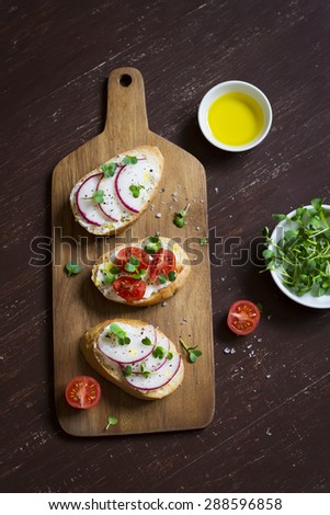 mini toast with radish, egg, arugula and tomatoes on dark blue wooden background