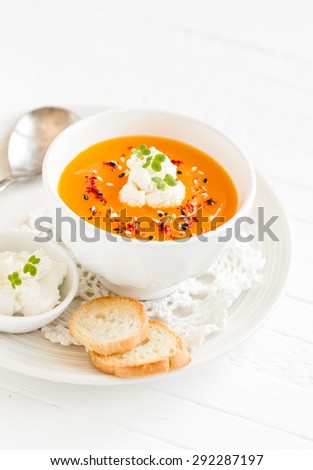 pumpkin soup with cream and paprika in a white bowl on a light wooden background