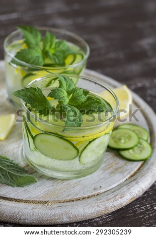 Lemonade with cucumber, lemon, mint and ginger in glass cups on a wooden surface
