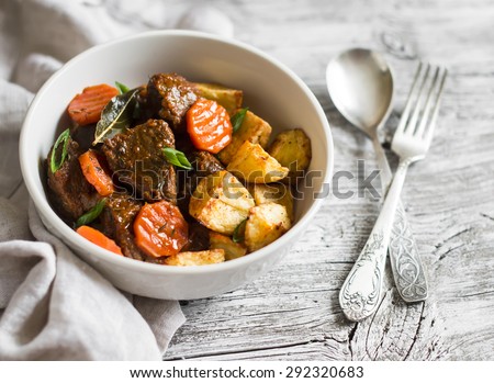 beef goulash with carrots and roasted potatoes in a white bowl on a light wooden background