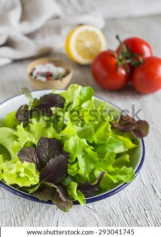 ingredients for salad - fresh lettuce, tomato and salad dressing on a light wooden background