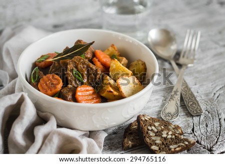 beef goulash with carrots and roasted potatoes in a white bowl on a light wooden background