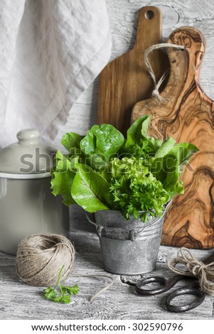 fresh herb salad in vintage metal bucket, olive cutting Board, old vintage scissors, twine, enamel container on a light wooden background
