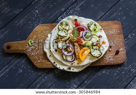grilled chicken breast, fresh vegetables - tomatoes, cucumbers, zucchini, onions, peppers and homemade tortilla on a dark wooden background