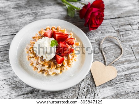 waffles with strawberries and vanilla ice cream, red rose and paper heart on a light wooden background
