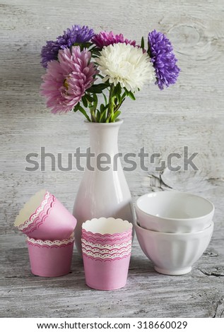 autumn flowers asters in a white vase, ceramic bowls and paper molds for baking cakes, still life in vintage style, on a white wooden surface