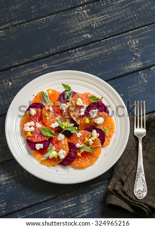 salad with beets, oranges and soft cheese on a white plate on a dark wooden background