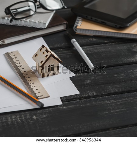 Planning of the construction of a house. Office desk with business objects - open notebook, tablet computer, glasses, ruler, pen and model of a wooden house. Free space for text. Office workplace