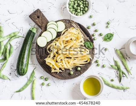 Dry pasta tagliatelle, zucchini, green beans and peas, olive oil on a light background. Vegetarian food