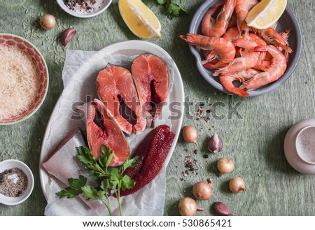 Ingredients for cooking lunch - fresh red fish, shrimp, rice, spices. On a wooden table, top view. Flat lay