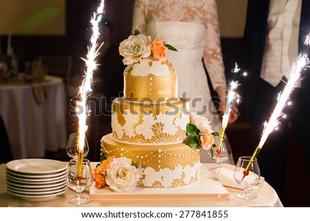 Big beautiful golden wedding cake with flowers next to bride and groom