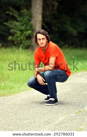 Male model in an orange shirt squatting on a path outside