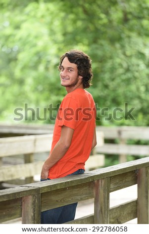 Male model with orange shirt leaning against bridge looking back