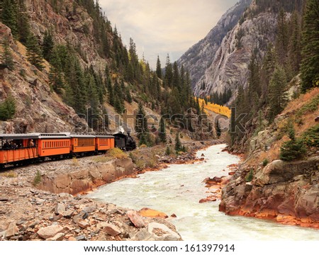 An antique steam engine and train traveling through the rocky mountains in the fall