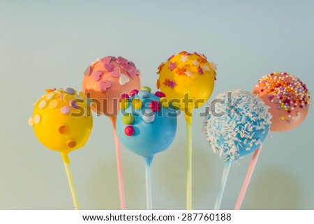 Blue pink and yellow pop cakes with brightly coloured an assortment of sprinkles, against a blue background.