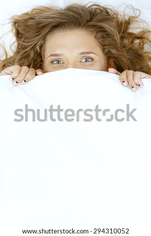 Funny young beautiful woman lying in bed under blanket