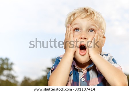 Child expressing surprise with hands on his face