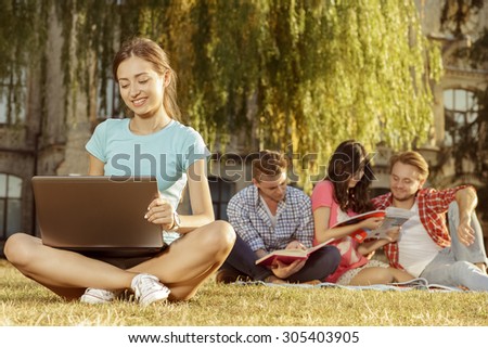 A group of beautiful young student sitting on the grass in the park and prepare for exams