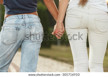 Two girlfriends holding hands. Back view.