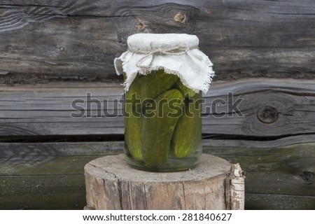 A glass jar of pickles standing on a wooden stand with wooden background