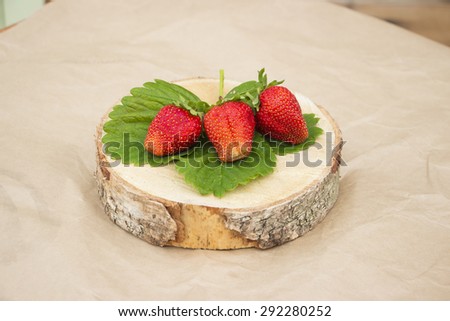 Three strawberries on a wooden cut on craft paper background side view