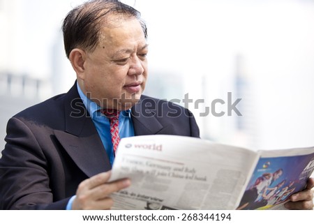Asian businessman in suit reading newspaper