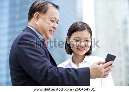 Asian businessman & young female executive looking at smart phone