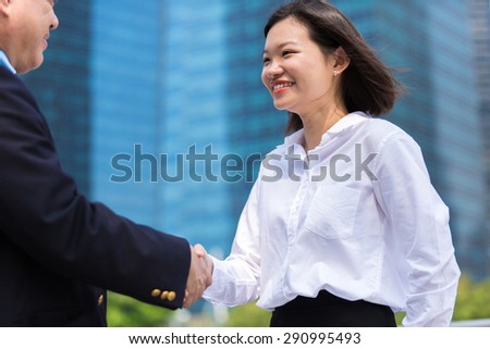 Asian businessman & young female executive shake hands