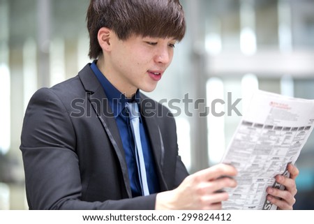 Young Asian male business executive reading newspaper