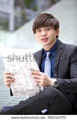 Young Asian male business executive reading newspaper