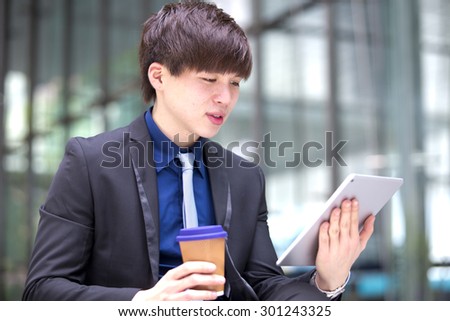Young Asian male business executive using tablet PC and holding coffee cup smiling