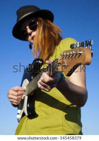 Stylish female street artist with guitar, focus on the hand in the middle of the guitar, blue sky on the background
