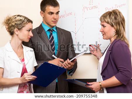 Business meeting. Discussion near wall mounted drawing board between business woman and customers.